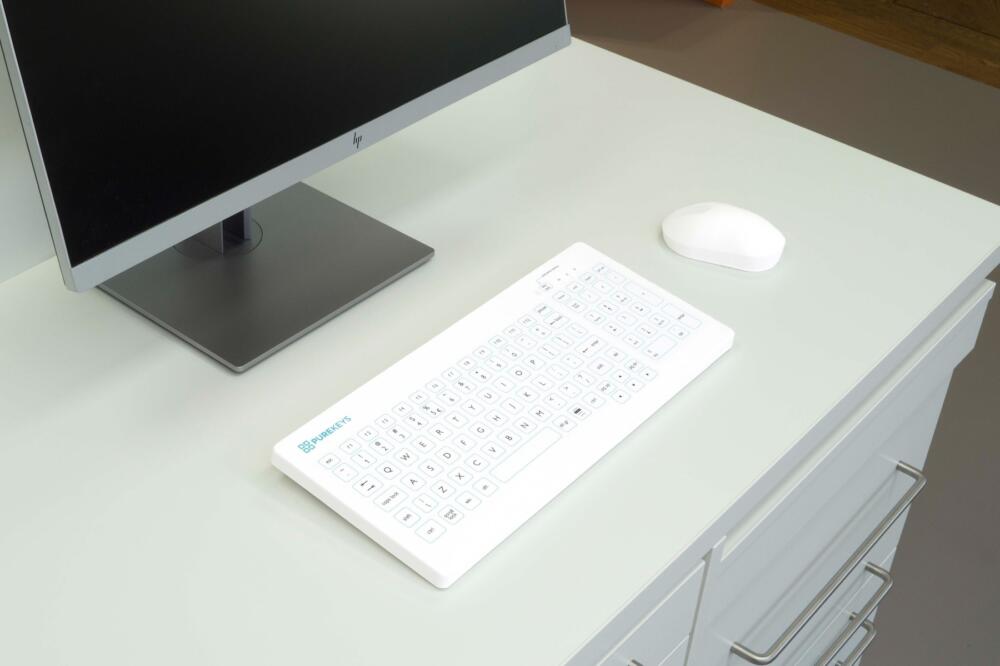 Purekeys medisch toetsenbord US wit op een medische werkplek, naast monitor en muis; vlak en eenvoudig te desinfecteren.
