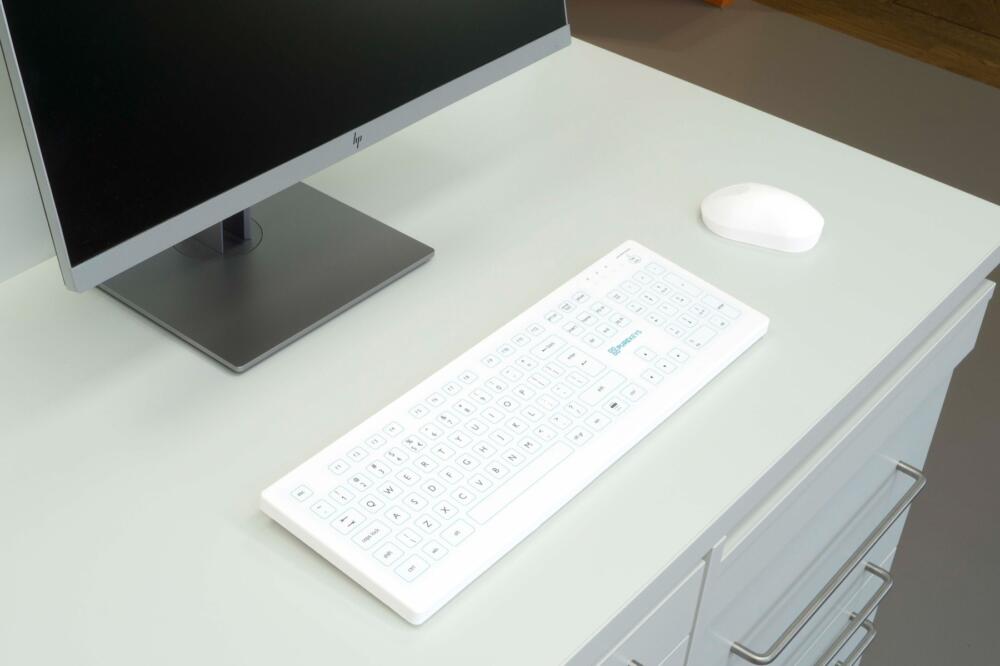 Purekeys medisch toetsenbord wit op een medische werkplek naast monitor en muis; hygiënisch vlak ontwerp met numeriek toetsenblok.